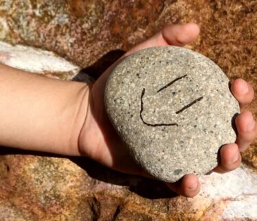 a hand holding a rock with a smiley face drawn on it