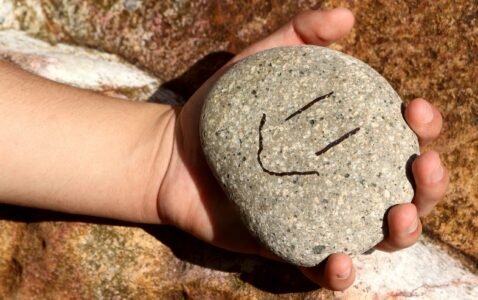 a hand holding a rock with a smiley face drawn on it